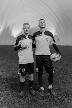 Monochrome image of two adult male soccer players in uniform indoors.