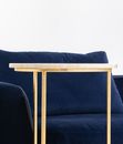 Part of comfortable blue sofa with cushion placed near golden round side table against white wall in light room