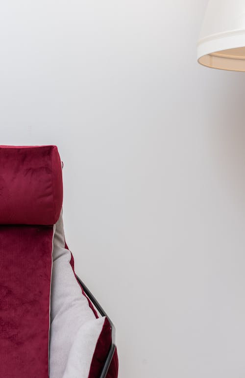 Detail of comfortable soft red armchair with armrest and part of white floor lamp placed on white background in light room