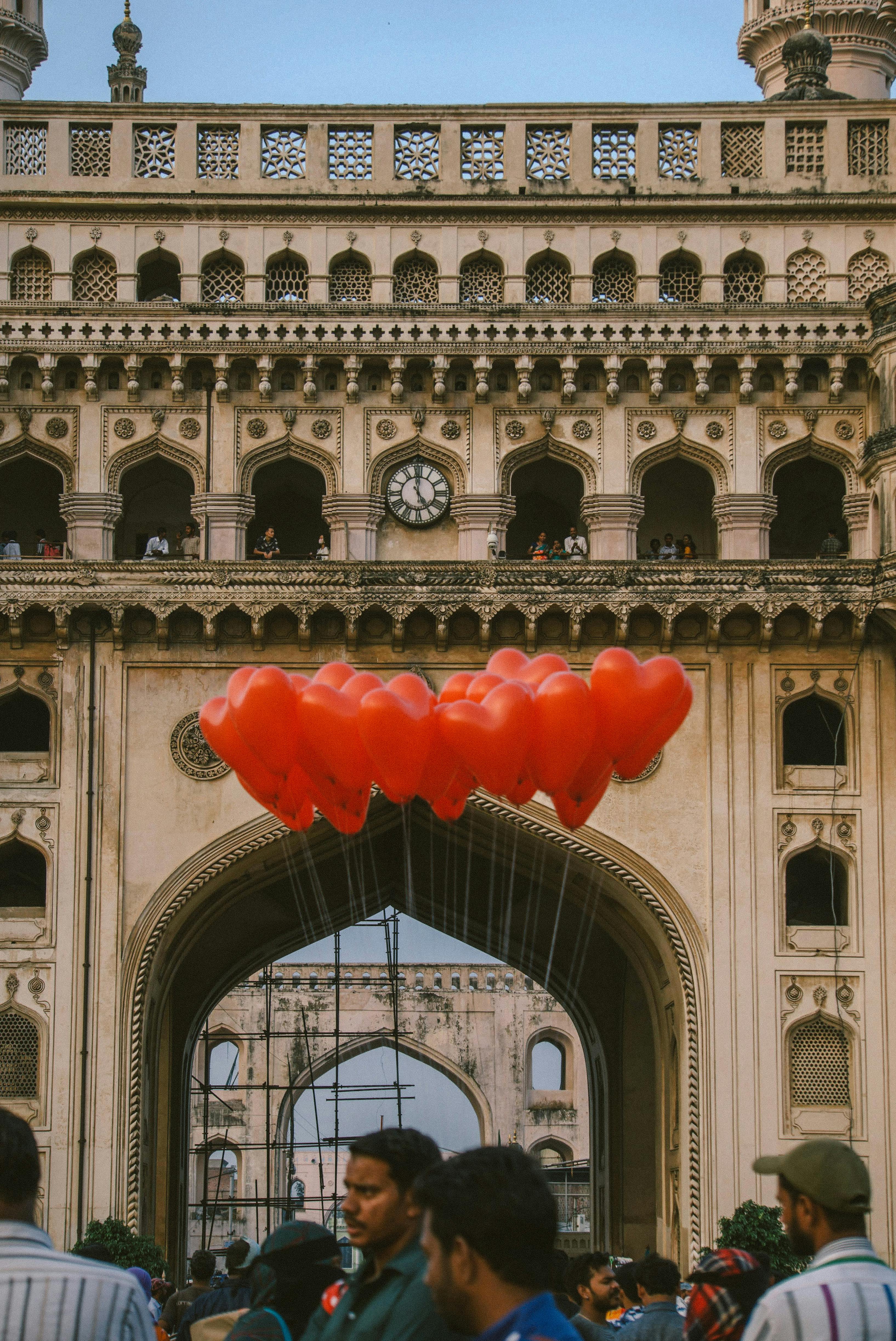 indian friends with red balloons against old city arches