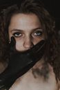 Creepy young female with dirty hand covering mouth on black background looking at camera