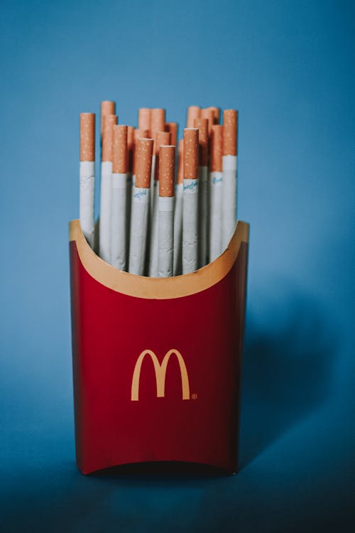 Red and yellow paper packet from french fries filled with cigarettes on blue background