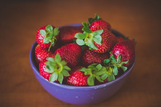 A vibrant bowl of fresh strawberries on a wooden table, perfect for healthy snacking.
