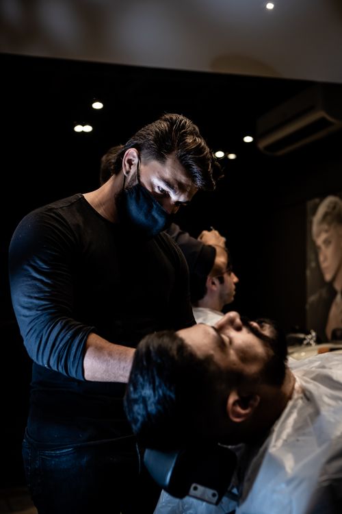 Free Barber wearing mask shaves client in a stylish barbershop for an elegant grooming experience. Stock Photo