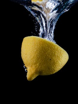 A fresh lemon half plunges into water against a black background, creating a dramatic splash.