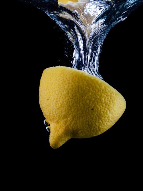 Free A fresh lemon half plunges into water against a black background, creating a dramatic splash. Stock Photo