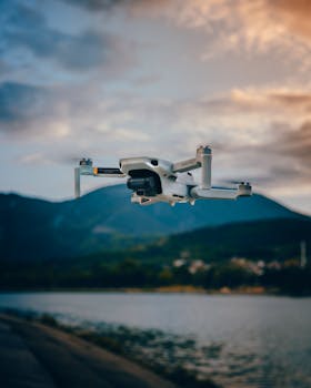 A white drone flying over a mountain lake with beautiful sunset clouds, showcasing nature and technology.