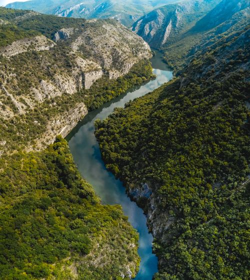 Free Aerial view of narrow curvy river flowing among rough rocky mountains and green trees Stock Photo