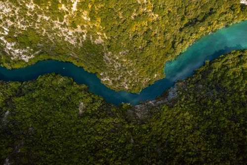 Free Top view of turquoise narrow river flowing among mountainous valley covered with green trees and grass Stock Photo