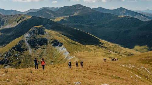 Picturesque landscape of rocky mountainous terrain covered with green grass with group of hiking travelers