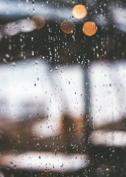 Close-up of raindrops on a window, creating a serene and moody atmosphere with a blurred urban background.
