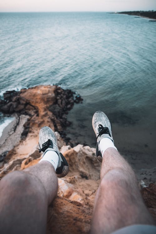 Free Person in Black and White Sneakers Sitting on Rock Near Body of Water Stock Photo