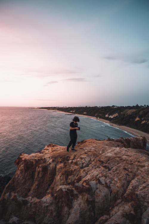 Free Photo of a Person in a Black Shirt Standing on a Cliff Near the Sea Stock Photo