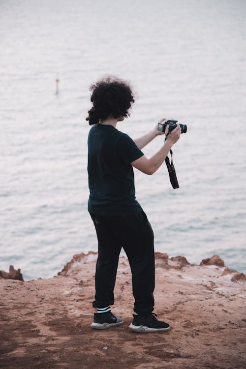 Free Photo of a Man in a Black Shirt Holding a Black Camera on a Cliff Stock Photo