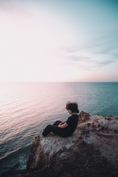 Free Photo of a Man with Curly Hair Sitting on a Cliff Near the Sea Stock Photo