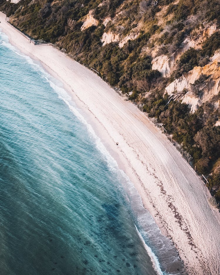 Drone Shot Of Sea Waves Crashing On A Shore With White Sand