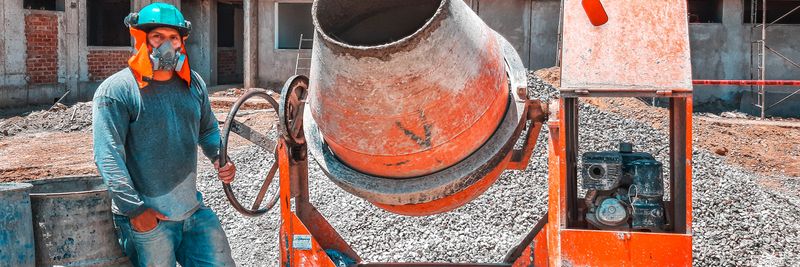 A construction worker operating a concrete mixer at an active building site, emphasizing safety gear.