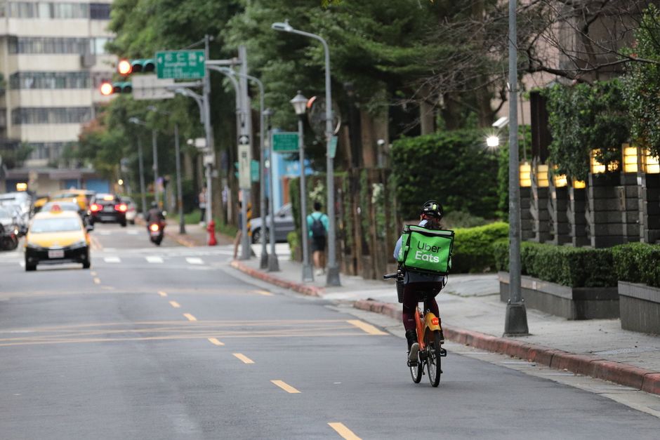 Uber Eats cyclist riding through Taipei's Xinyi District in daylight.