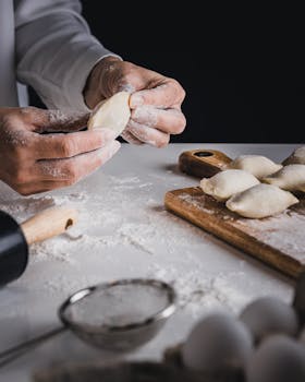 Chef prepares pierogi by hand, showcasing skills in a flour-covered kitchen setting.
