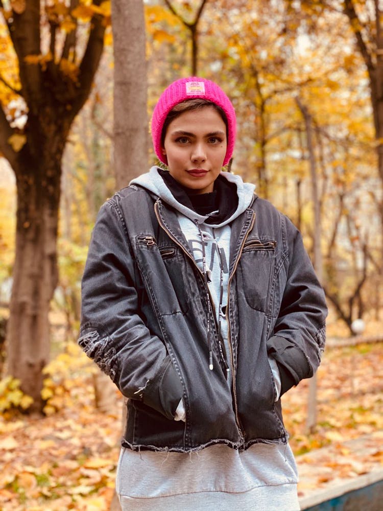 Woman In Zip Up Denim Jacket And Pink Knit Cap Standing Near Trees