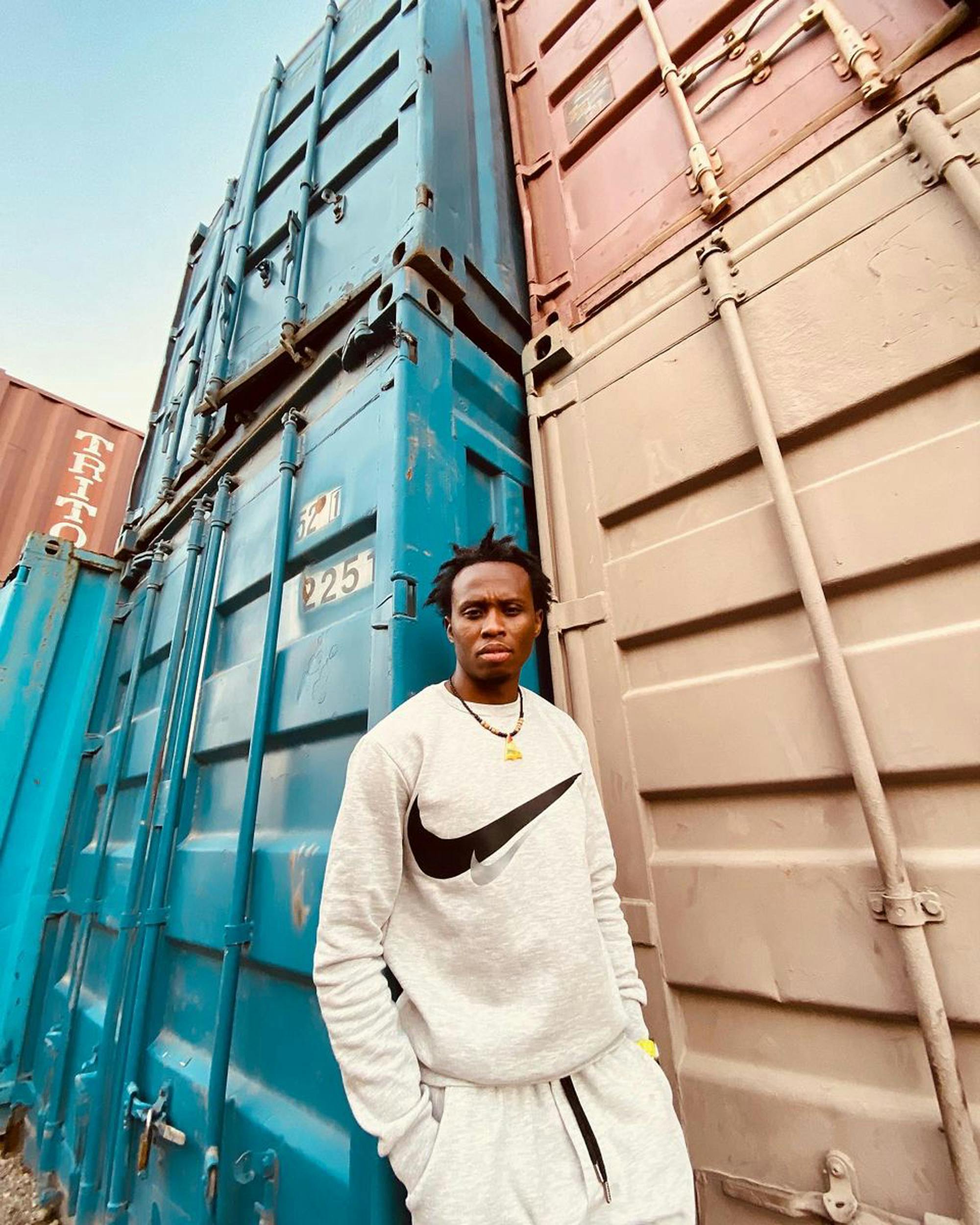 man in white terno jogger standing beside blue cargo container