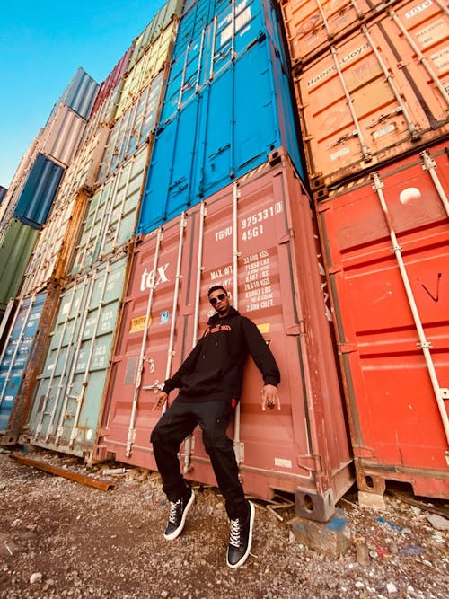 Man in Black Jacket Standing Beside Brown Shipping Container