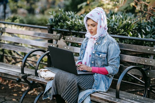 Serious Muslim woman working on laptop in park