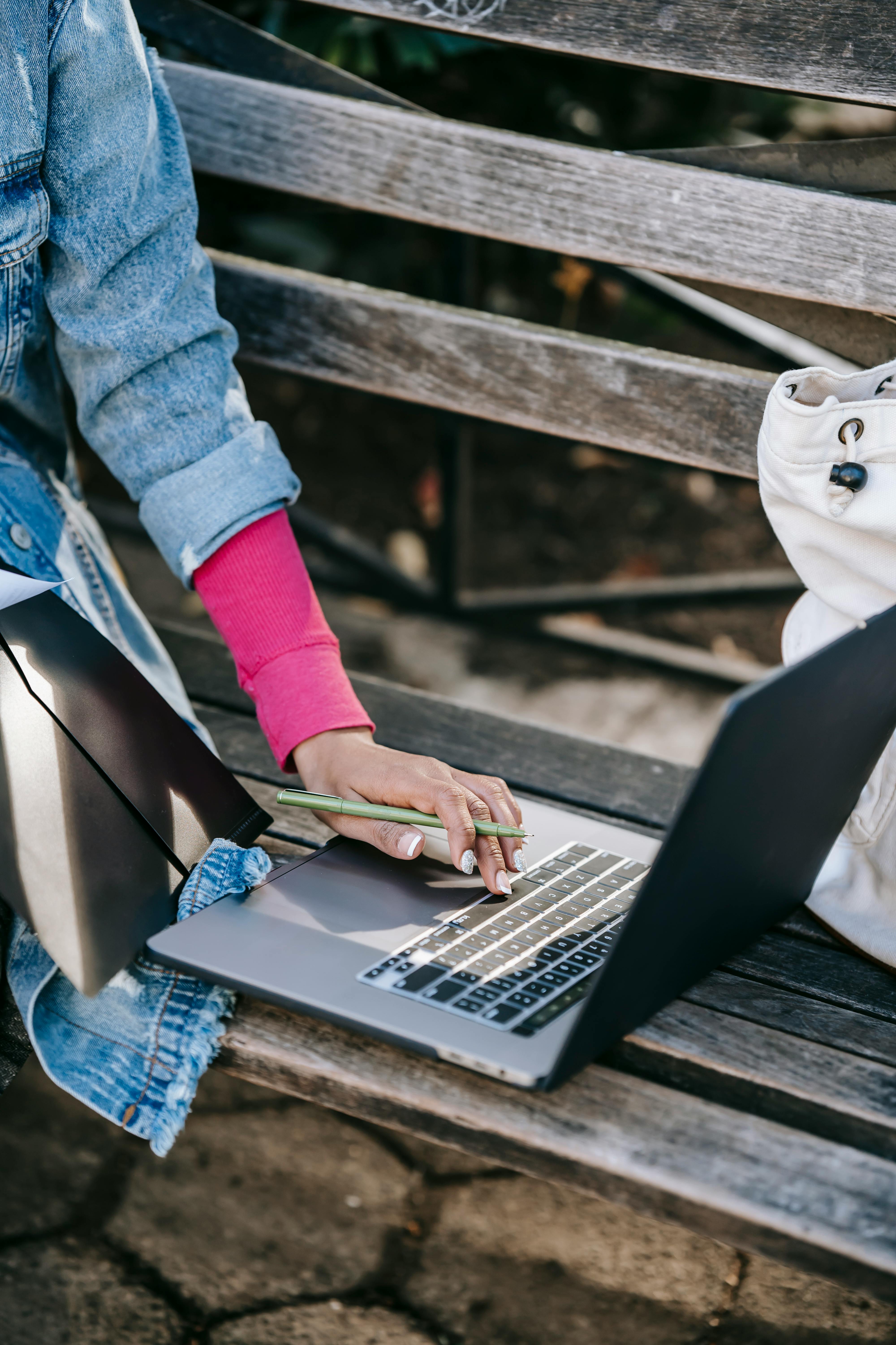 crop woman studying on laptop while sitting on bench in park