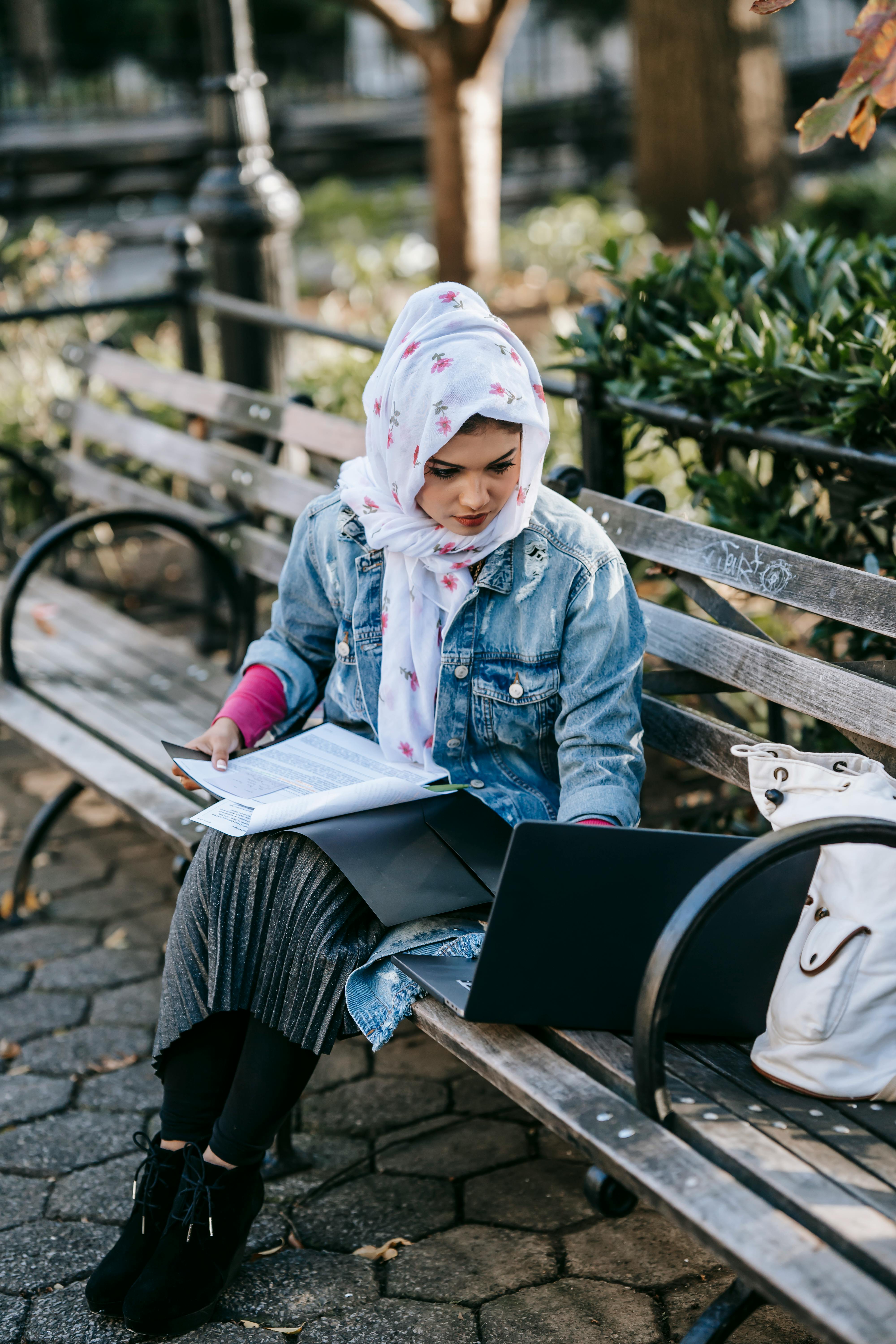 young ethnic woman typing on laptop in park