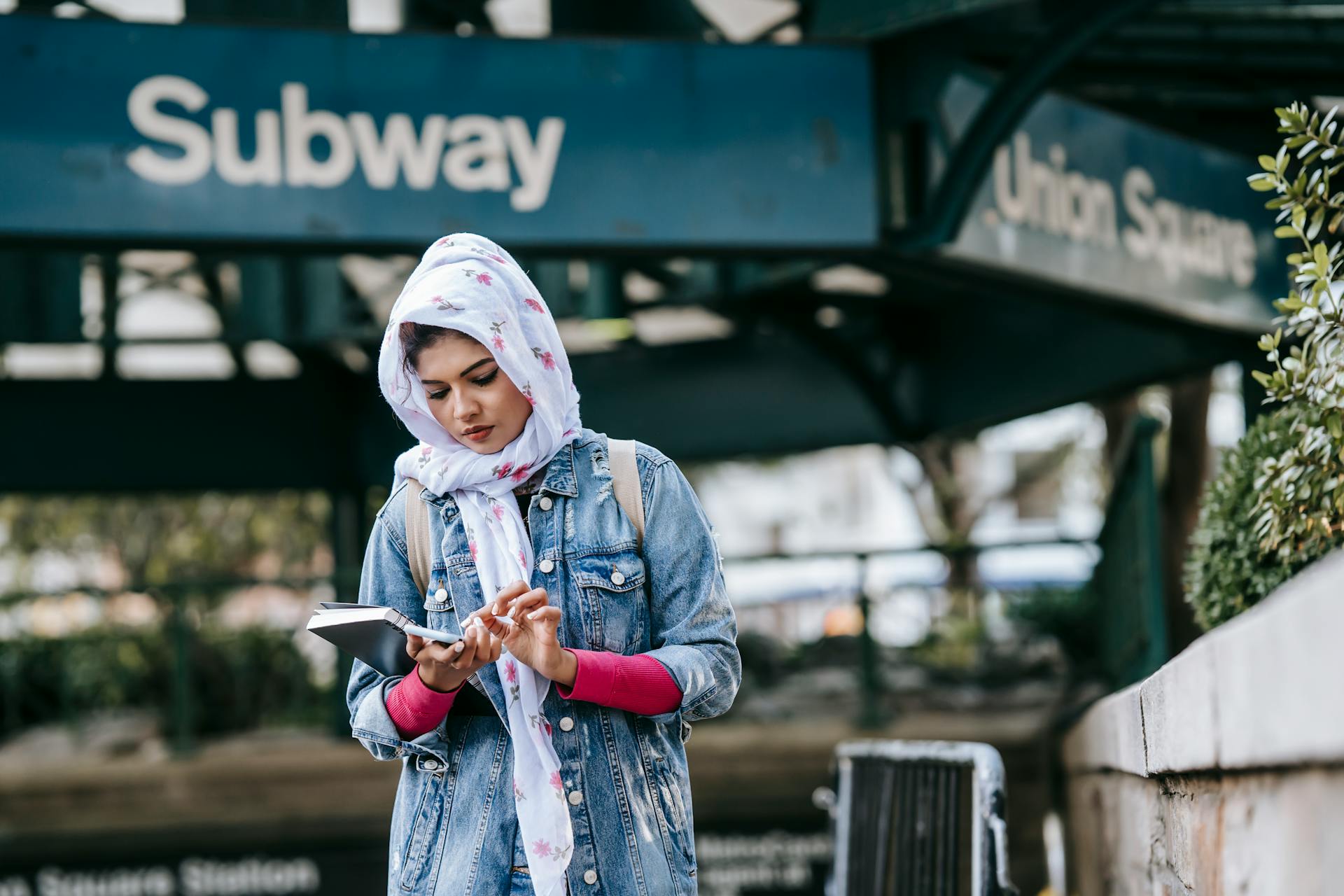 A young woman in hijab using her smartphone near Union Square subway entrance. Urban lifestyle scene.