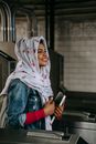 Smiling ethnic woman with copybook wearing hijab entering subway