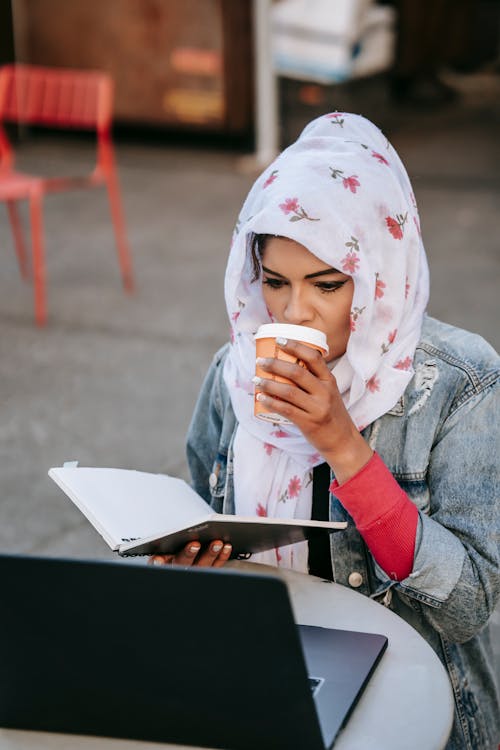 Young ethnic woman drinking coffee and comparing information