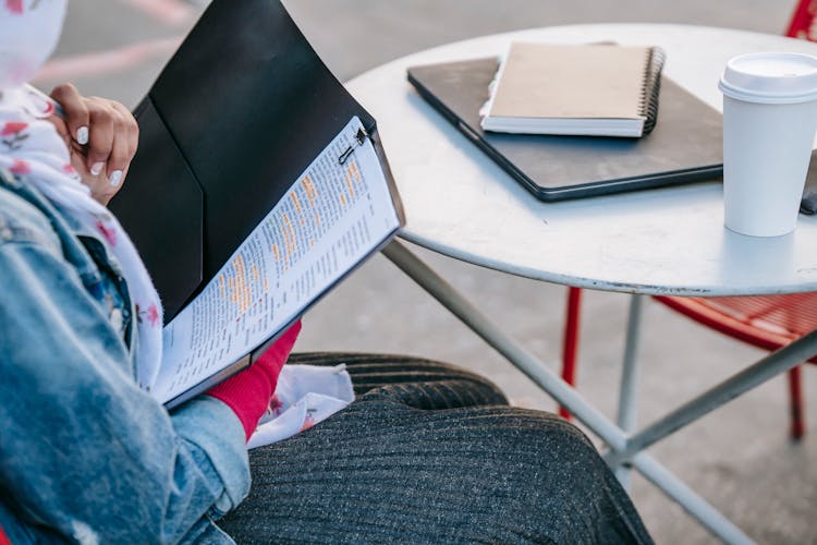 Student Sitting At Table And Reading Report In Folder In Daytime