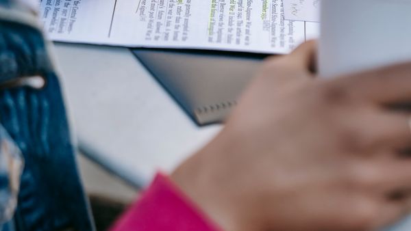 A person studying documents with notes, holding a coffee cup, in a casual setting