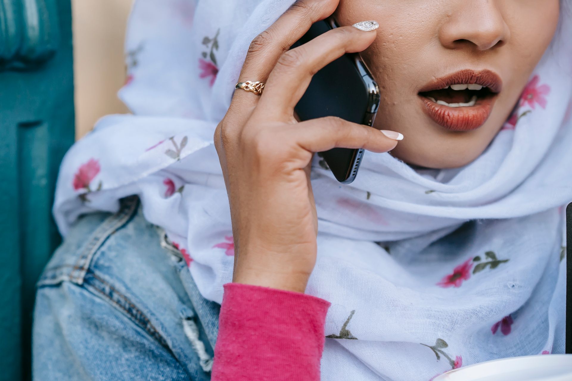 Close-up of a Muslim woman wearing a floral headscarf and talking on a smartphone outdoors.