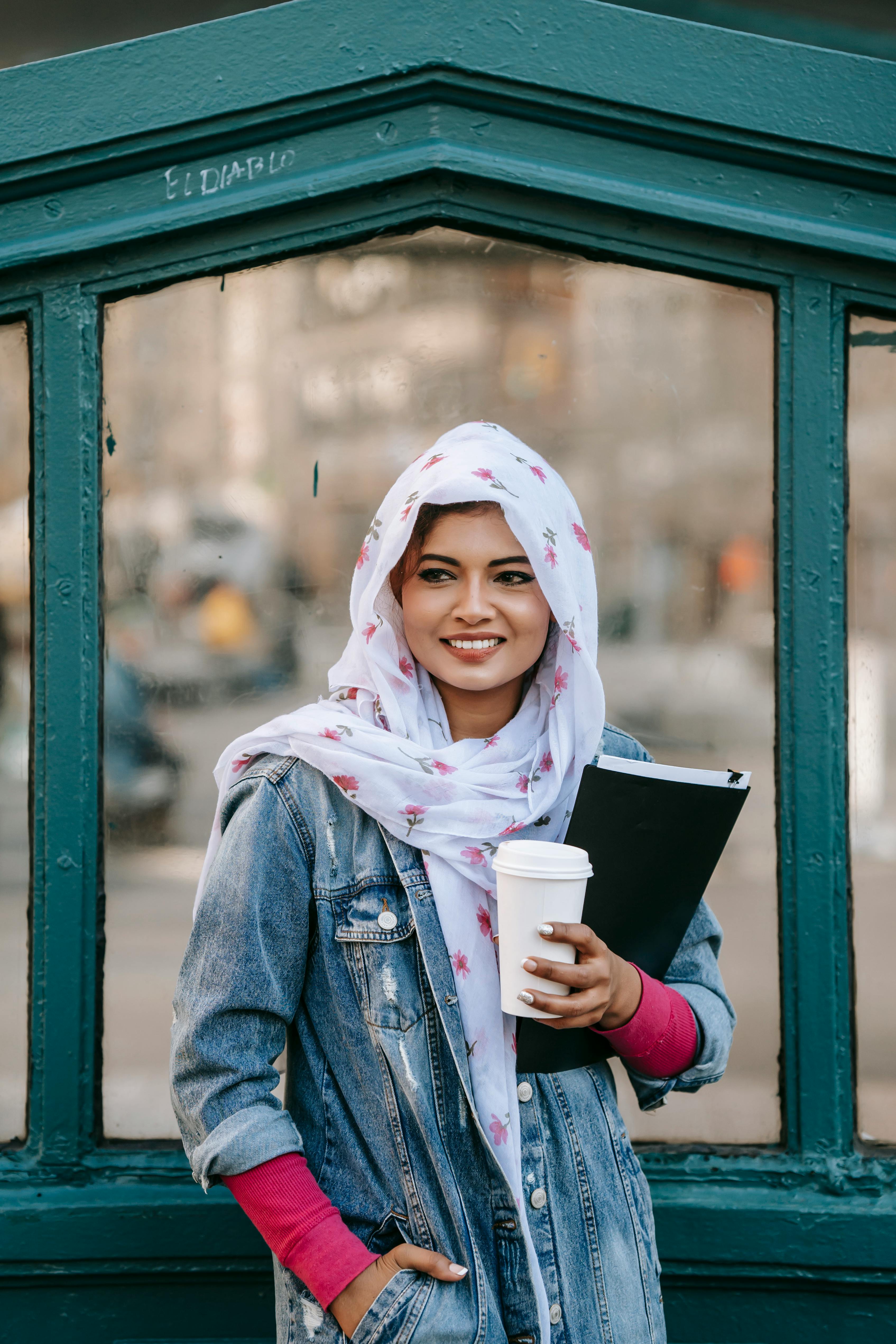 smiling muslim woman with documents in folder and takeaway cup