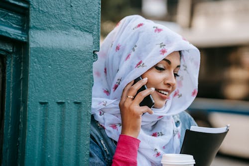 Smiling ethnic woman talking via modern smartphone in city street