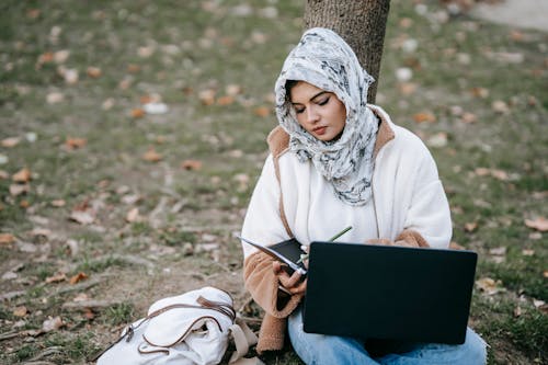 Focused woman in hijab working with documents and laptop in park