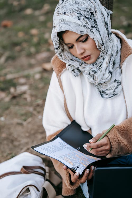 Concentrated ethnic woman in hijab writing notes in project