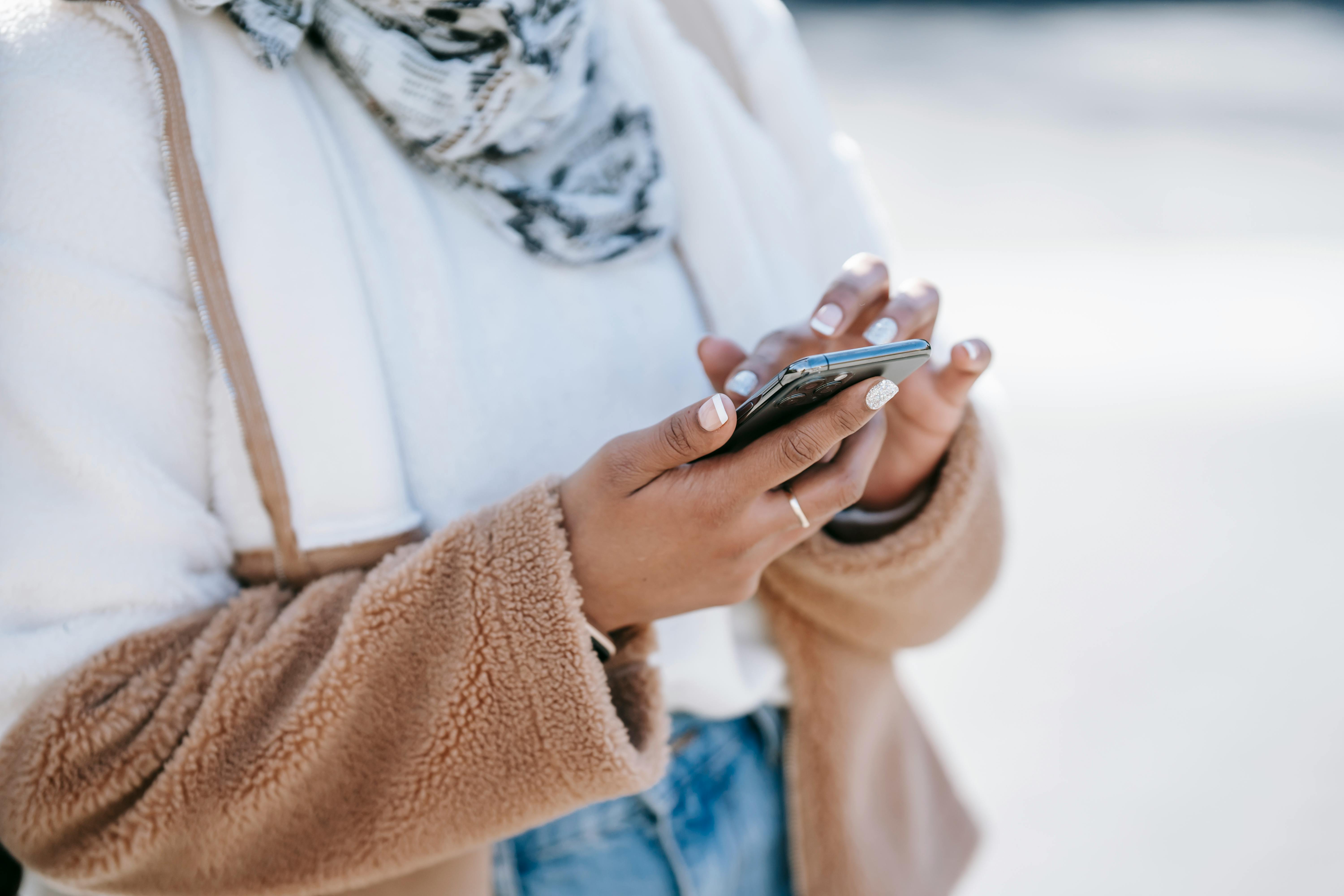 crop woman in warm jacket using smartphone in street