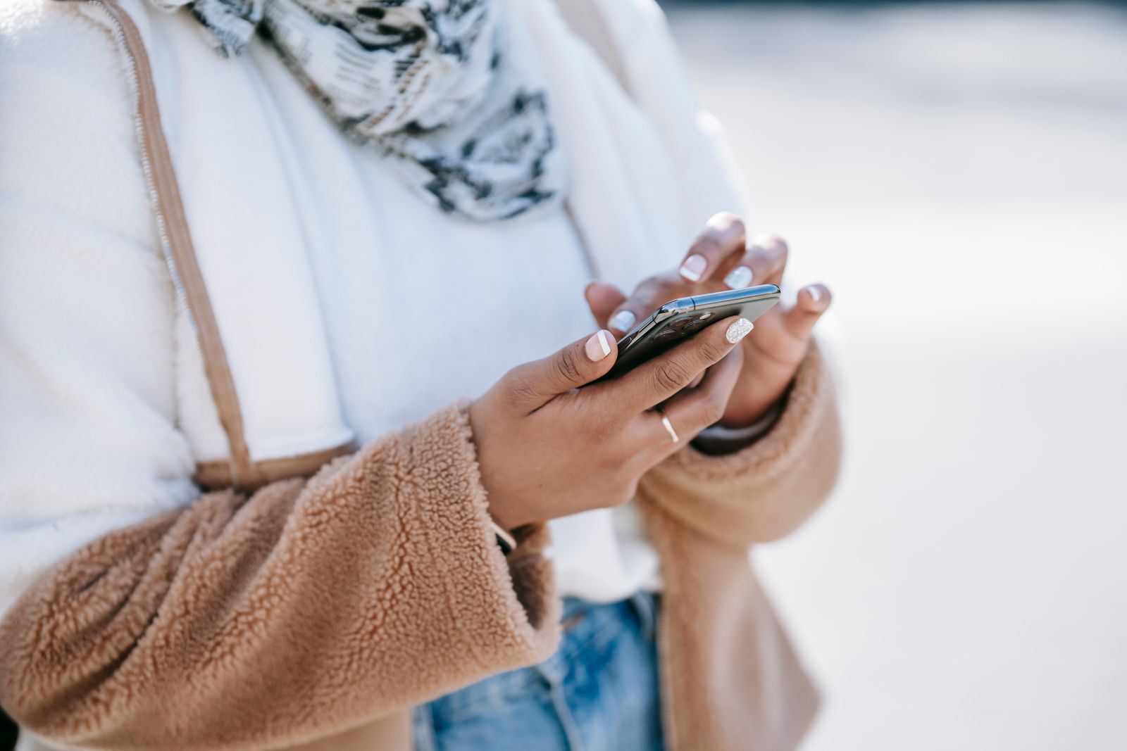 Woman in a cream and tan fleece jacket and patterned scarf holding a smartphone in bright sunlight