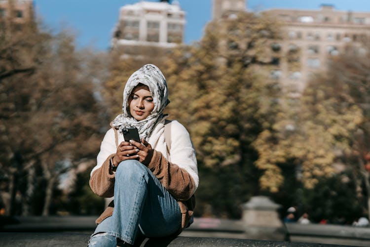 Young Ethnic Woman Using Smartphone While Sitting In City Park