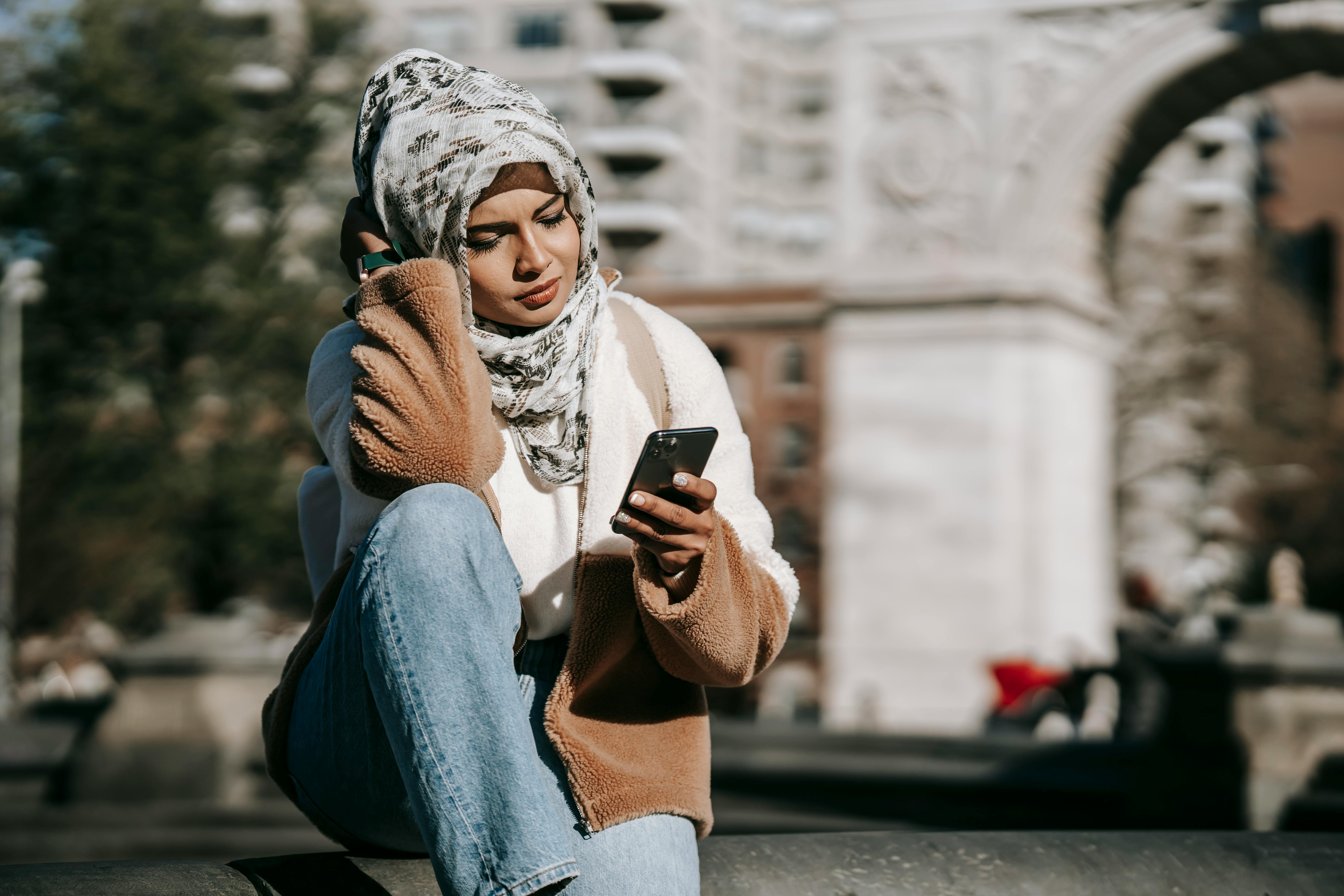 relaxed young muslim woman using smartphone on city street