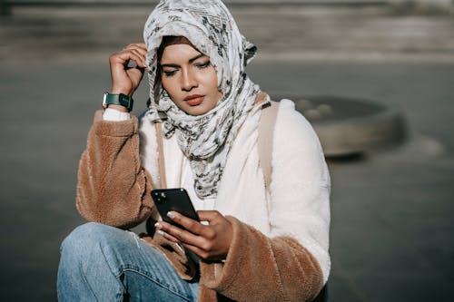 Free Stylish young ethnic lady in hijab using mobile phone on street Stock Photo