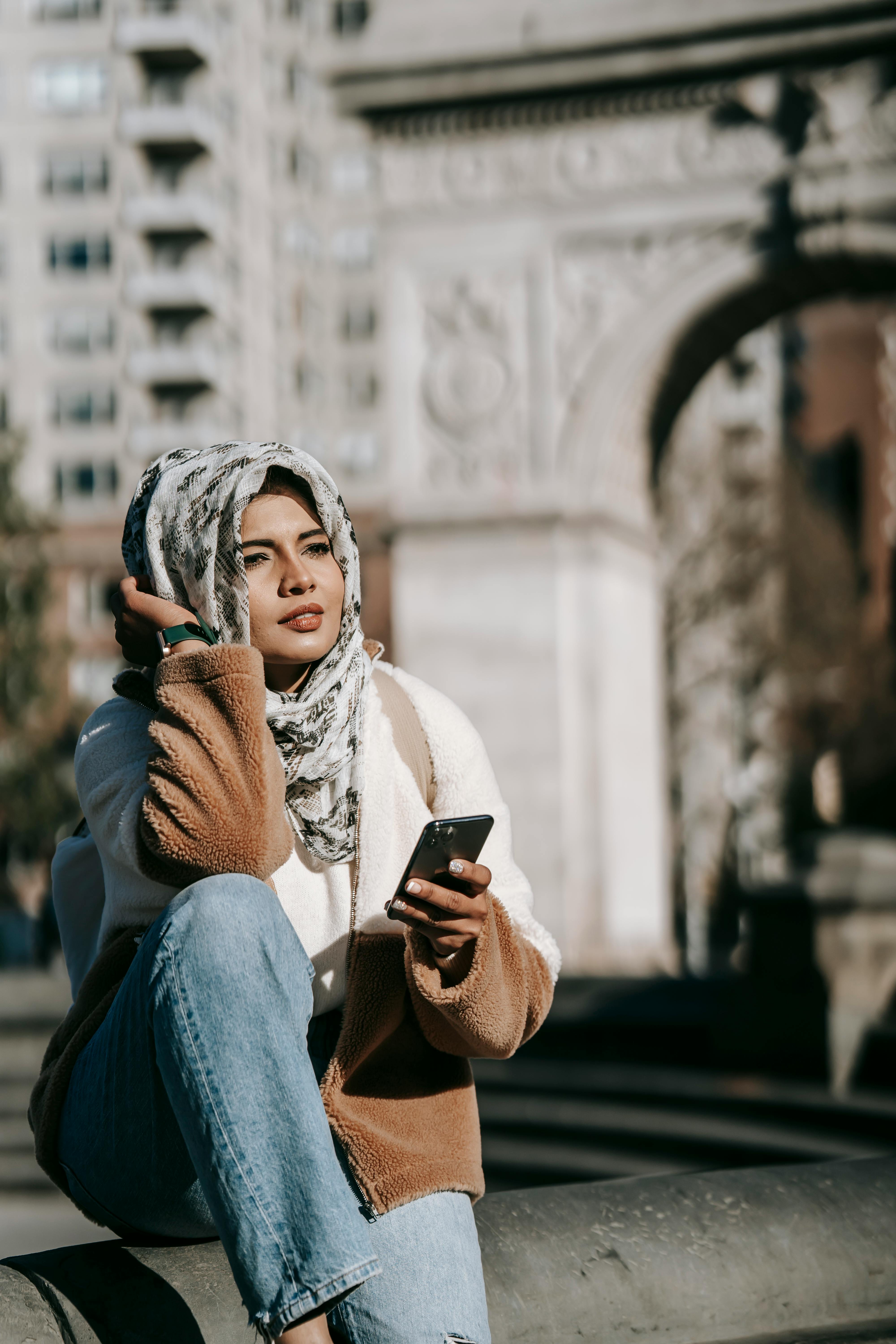 positive young arab woman relaxing on square and messaging on smartphone