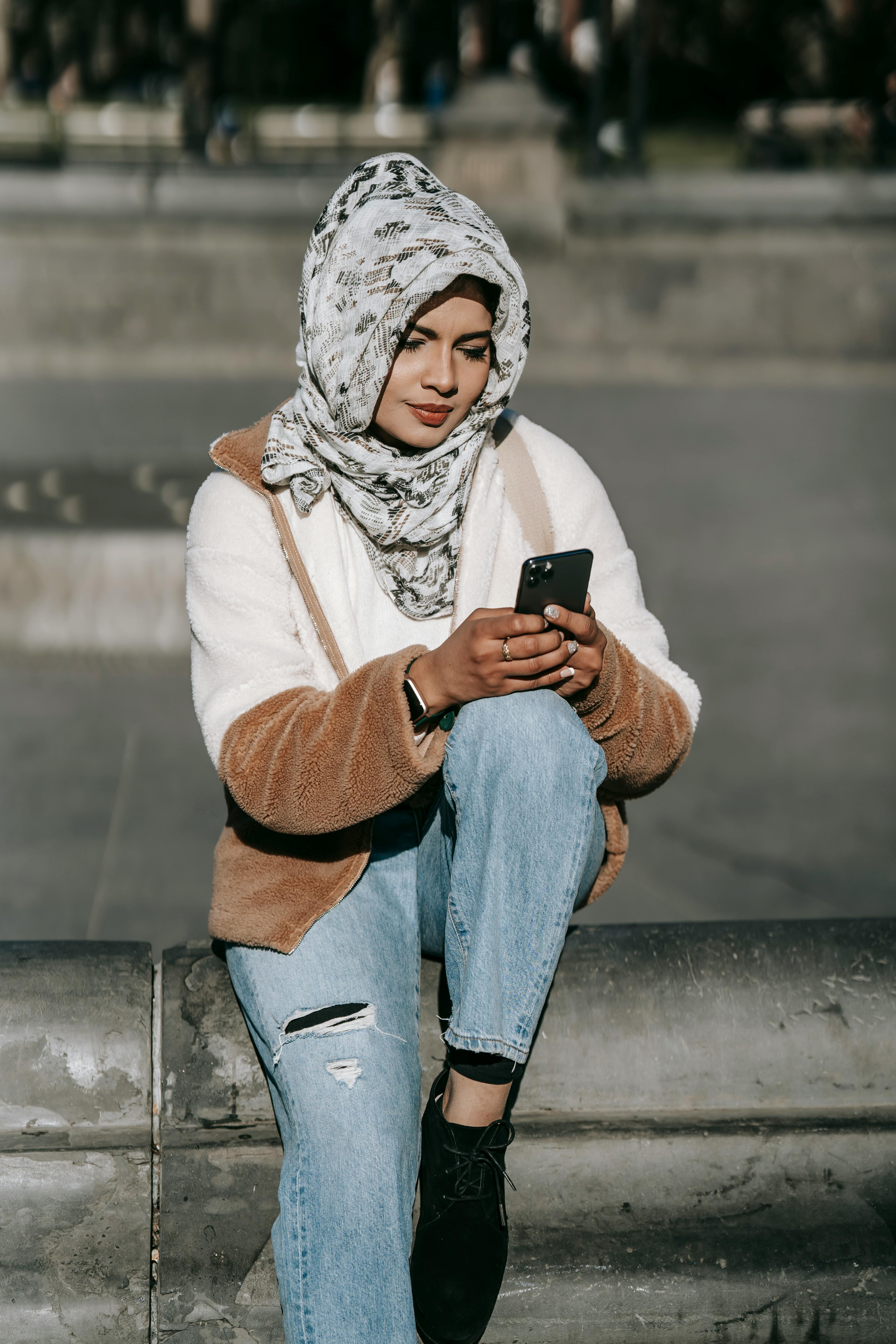 gorgeous young muslim woman surfing smartphone while resting on city square