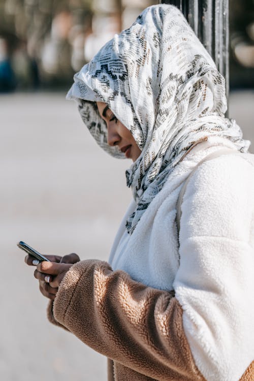 Stylish young Muslim woman browsing smartphone standing on street