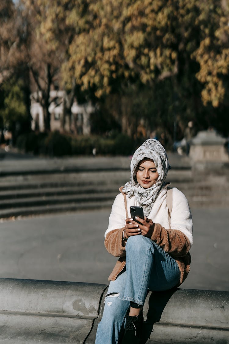 Content Young Ethnic Lady Messaging On Mobile Phone In Autumn Park