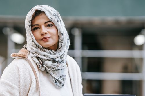 Free Calm young Muslim lady in elegant hijab and warm outerwear standing on city street and looking at camera Stock Photo