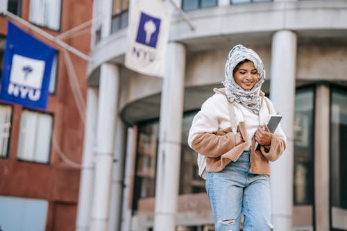 Delighted young ethnic female millennial standing near university building after studies